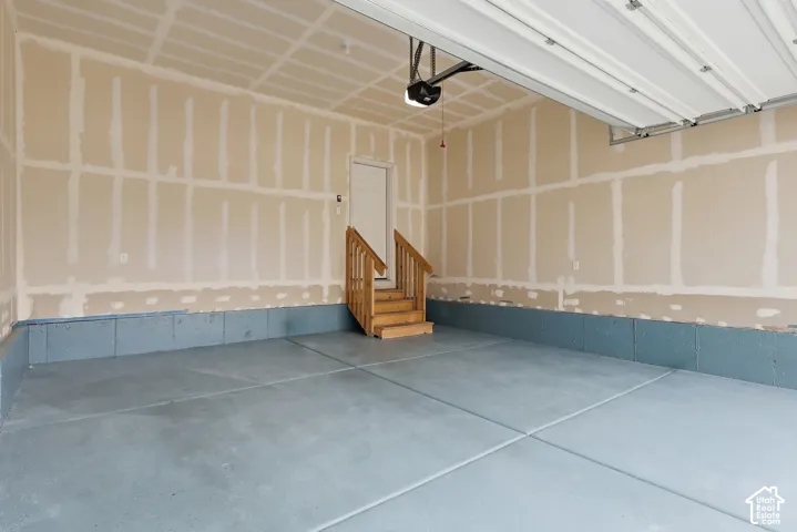 Attached garage with an automatic door opener, concrete flooring, and a wooden stairwell leading to an interior door