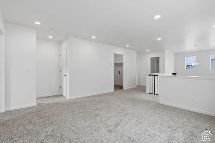 Spacious open area featuring recessed lighting, light-toned carpeting, and a stairway with black metal balusters