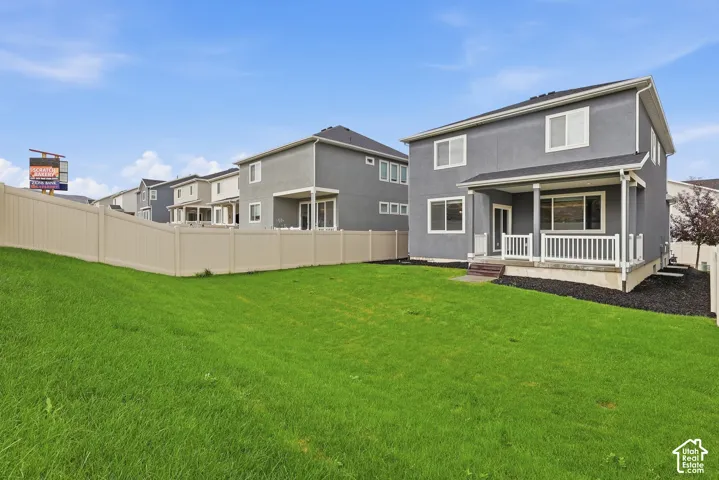 Expansive backyard with a manicured lawn, a full-height privacy fence, and a covered patio with white railings