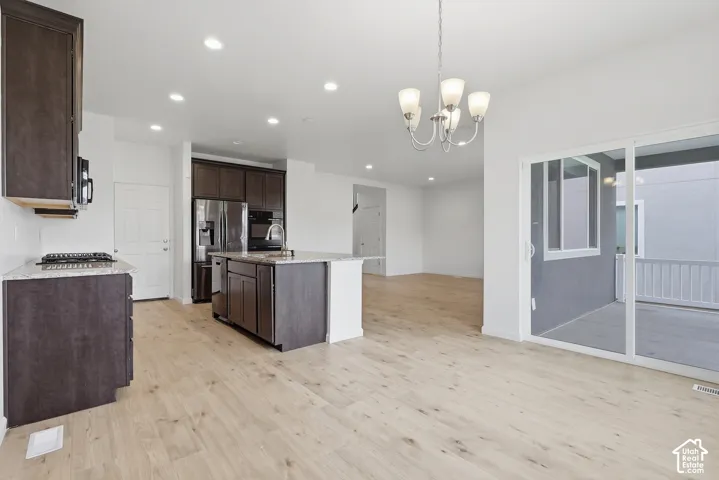 Open-concept kitchen with dark wood-finish cabinetry, a central island featuring a stainless steel sink, and light-toned wood-finish flooring