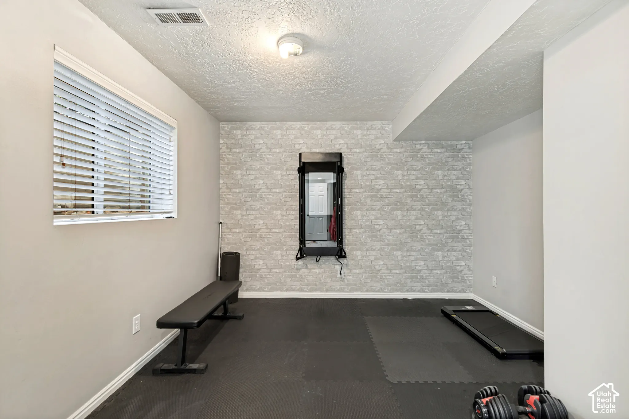 Recessed lighting illuminates the space, featuring a window with horizontal blinds and a textured accent wall
