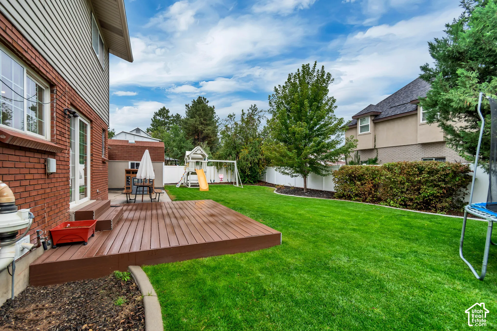 Expansive backyard featuring a manicured lawn, a brown composite deck with multiple steps, and a white privacy fence