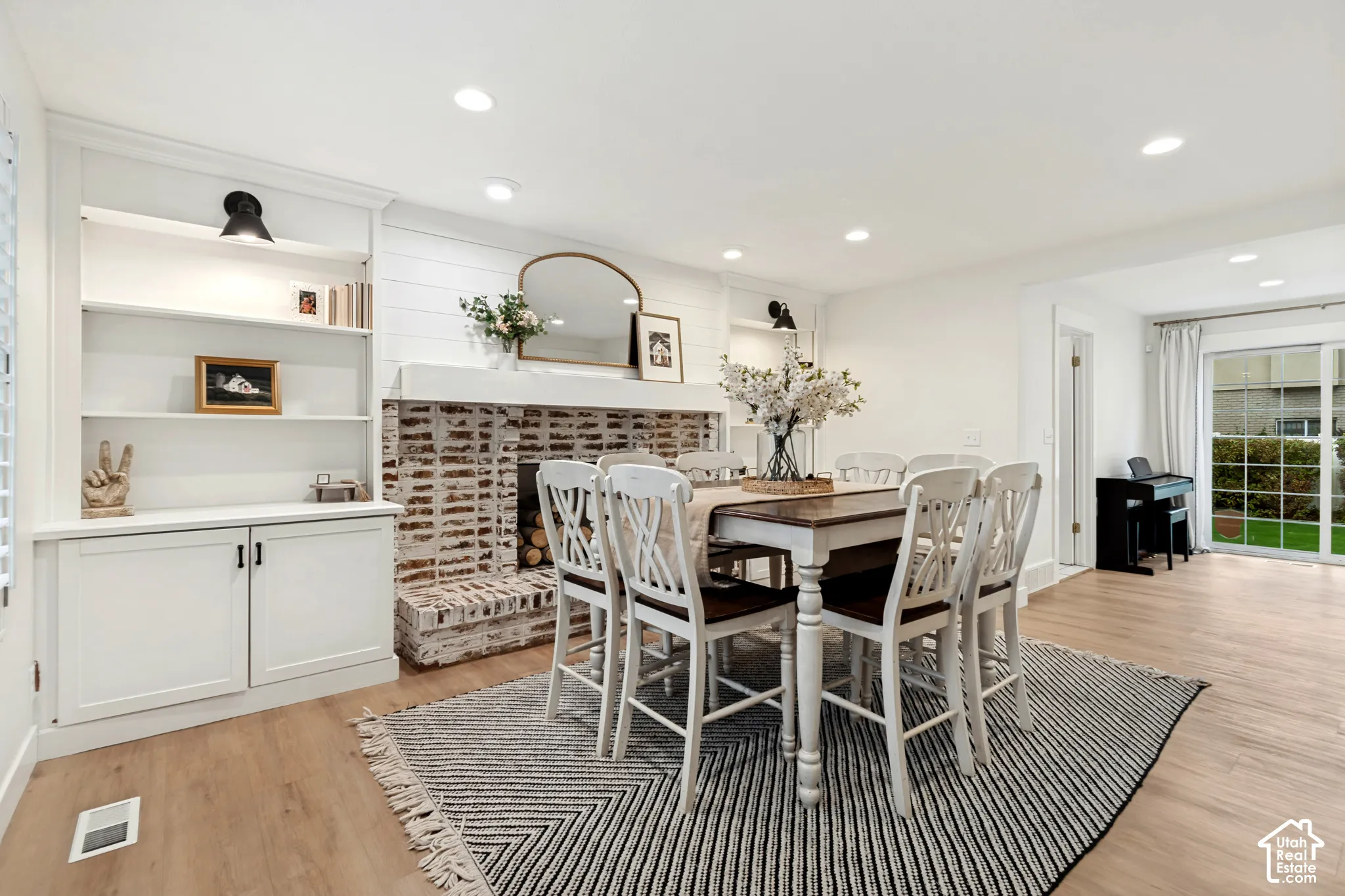 Built-in shelving with cabinetry, exposed brick fireplace, wood-finish flooring, recessed lighting, and sliding glass door