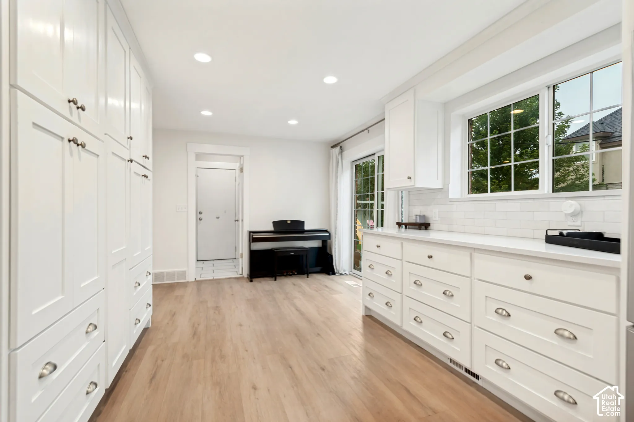 White cabinetry with ample storage, light wood-finish flooring, white subway tile backsplash, and sliding glass door