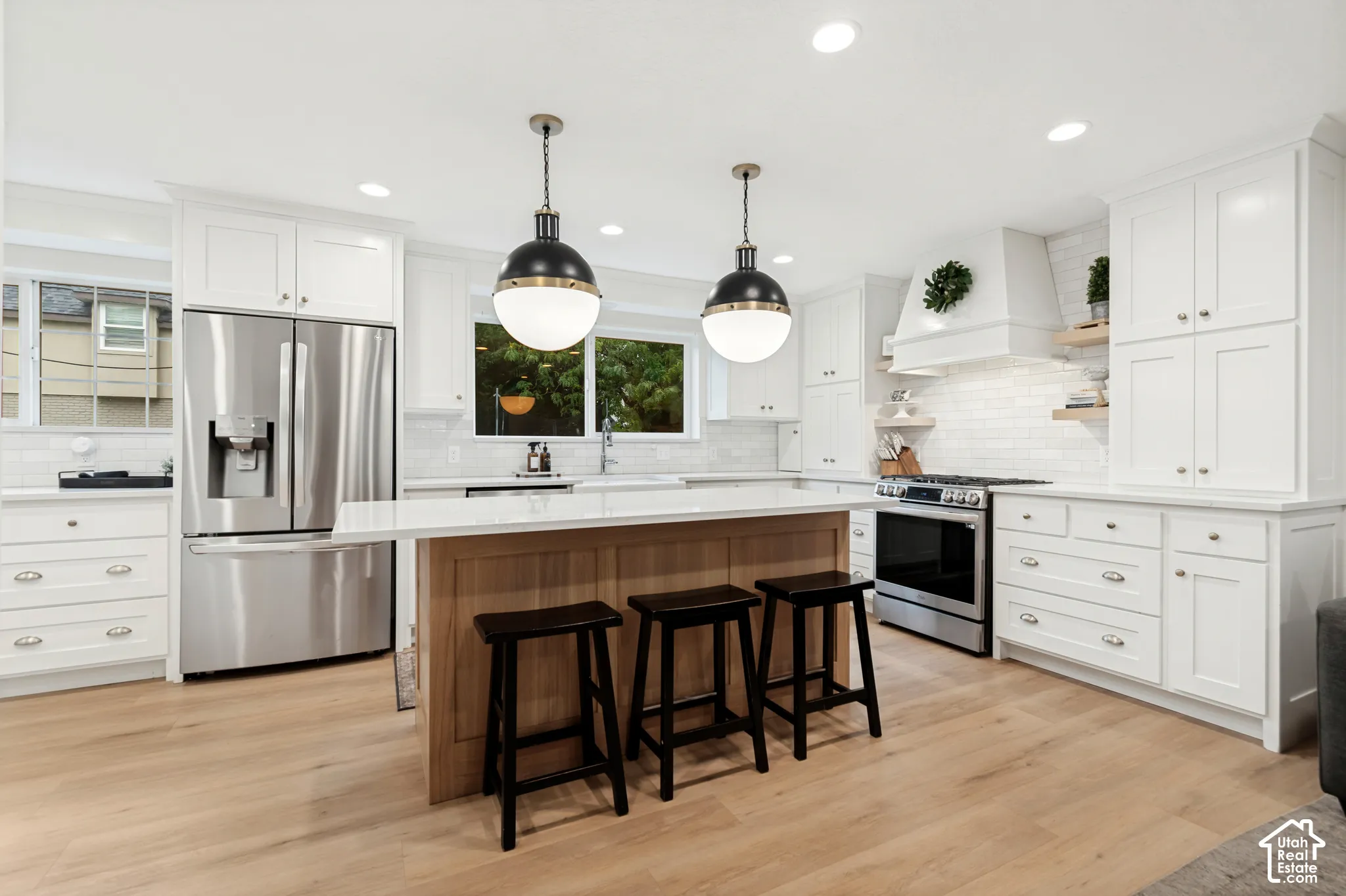Modern kitchen featuring white cabinetry, stainless steel appliances, a center island with bar seating, wood-finish flooring, and pendant lighting