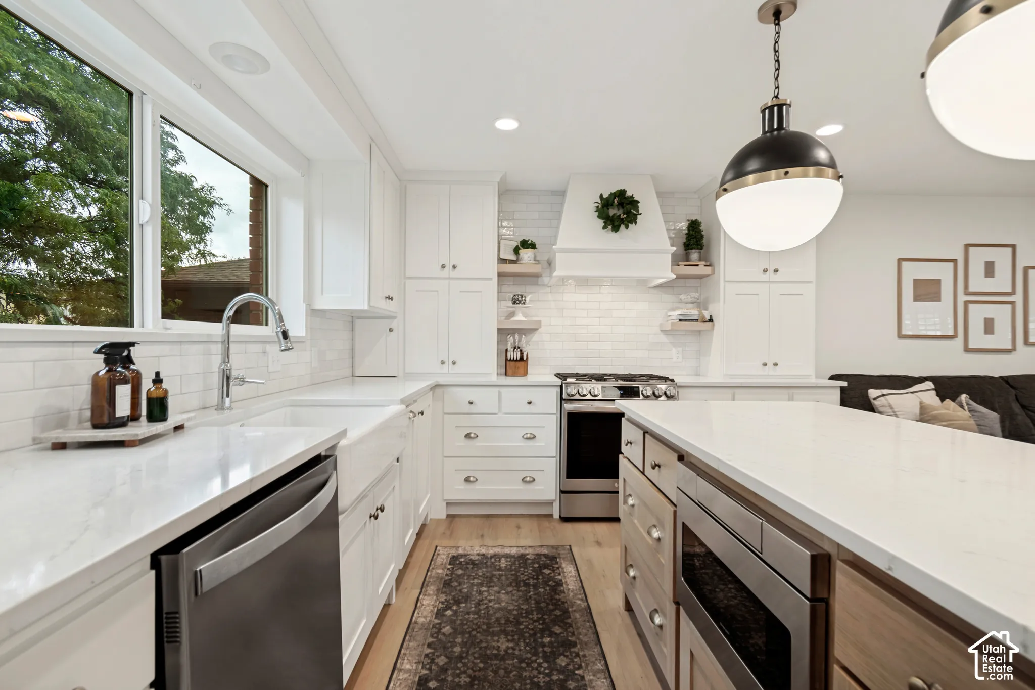 White cabinetry, stainless steel appliances, light wood-finish flooring, white subway tile backsplash, and a large central island