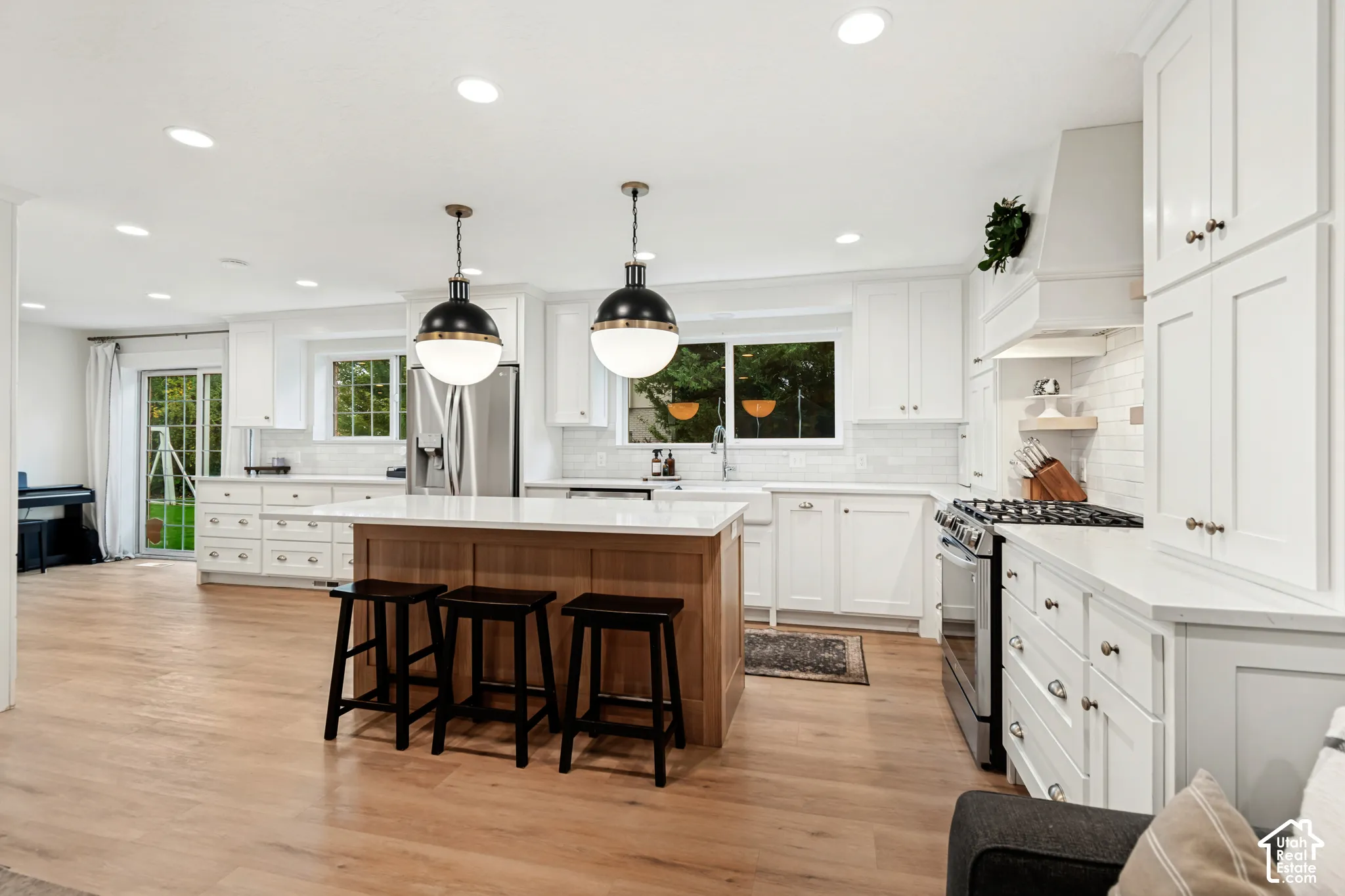 Kitchen featuring a substantial wood-finish island, white cabinetry, integrated stainless steel appliances, and wood-finish flooring