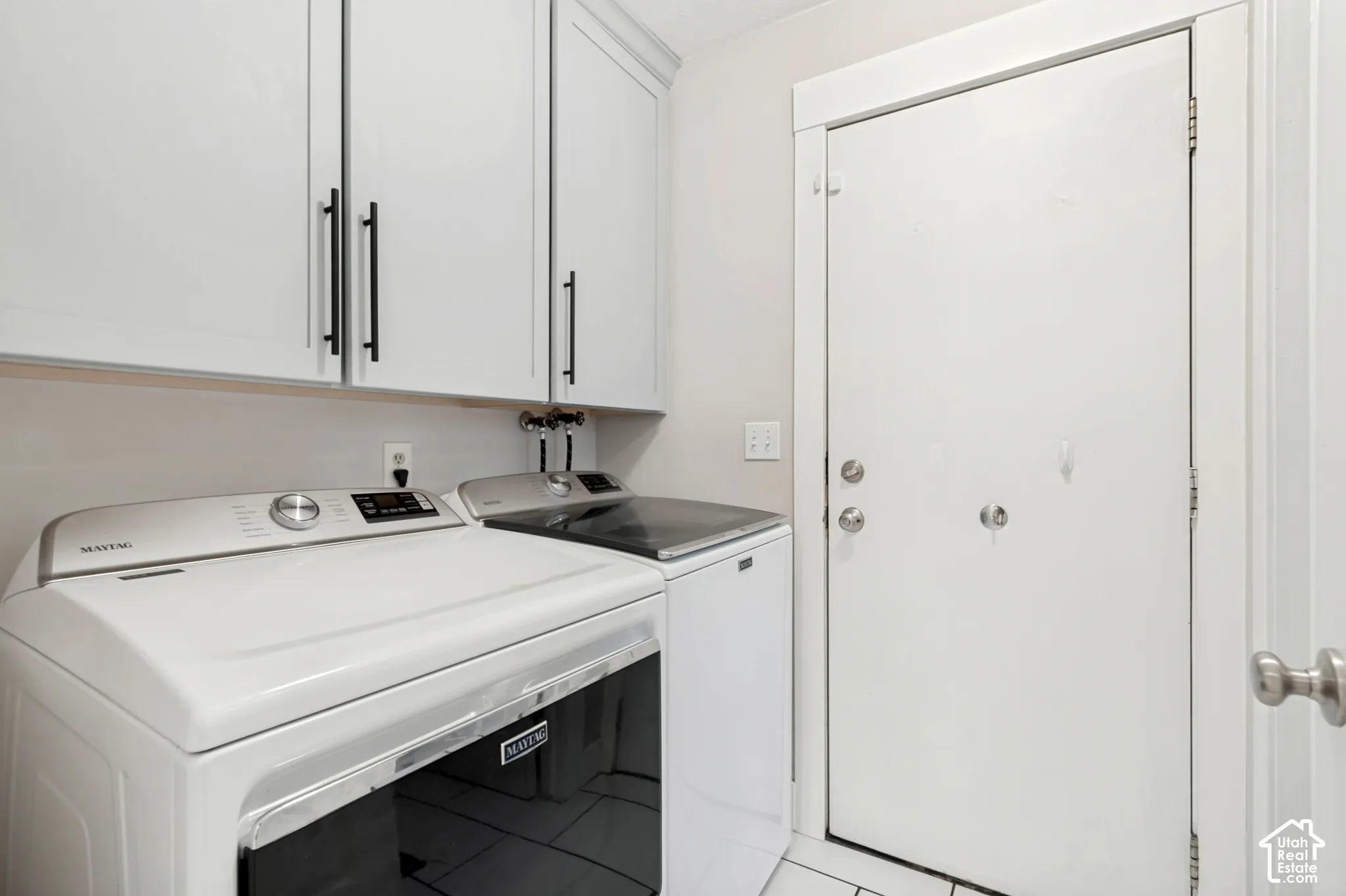 Laundry area featuring overhead cabinetry with matte black pulls, light-toned walls, and a white door with silver-toned hardware