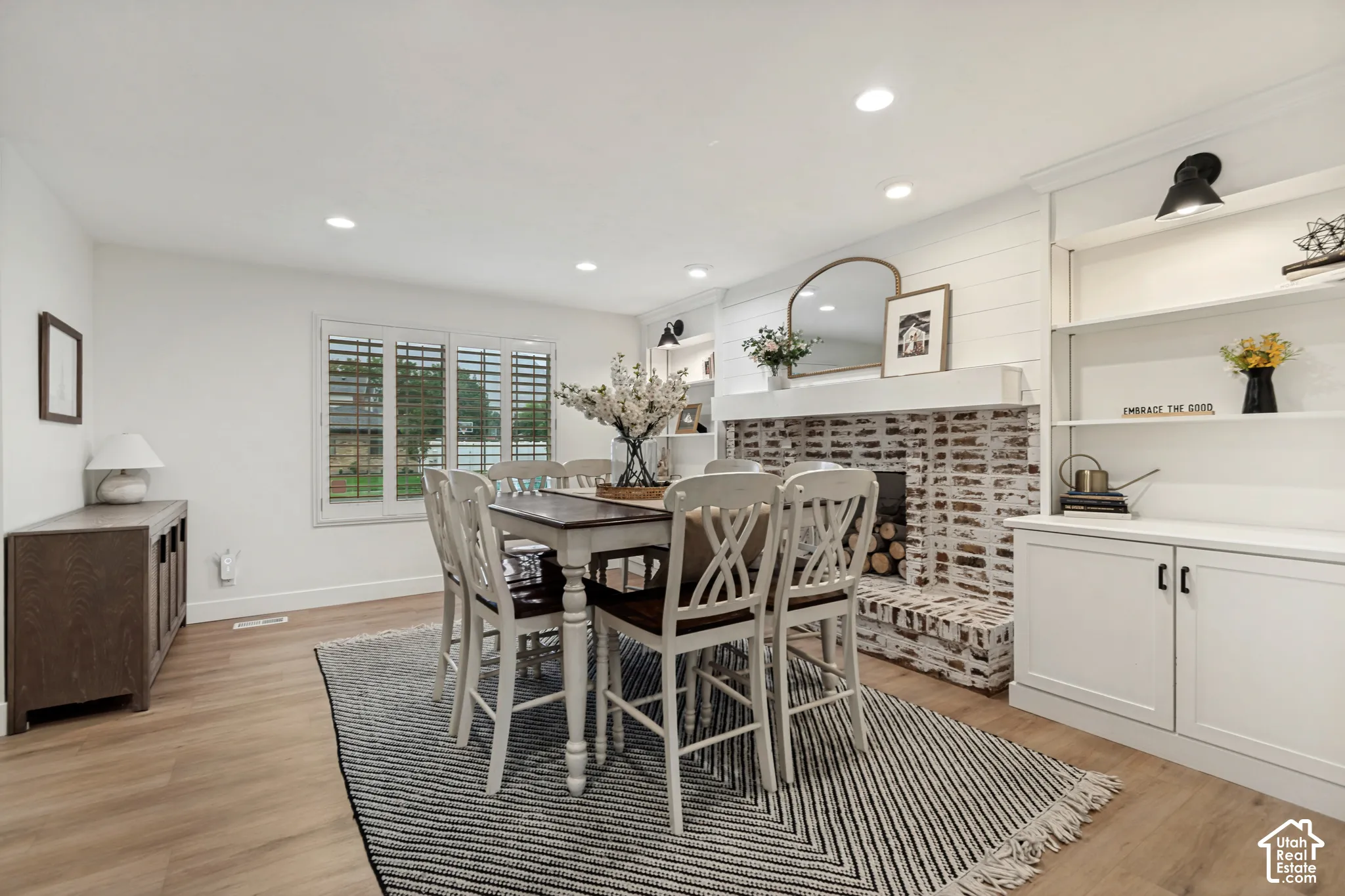 Recessed lighting, wood-finish flooring, white brick fireplace, built-in shelving, and white plantation shutters