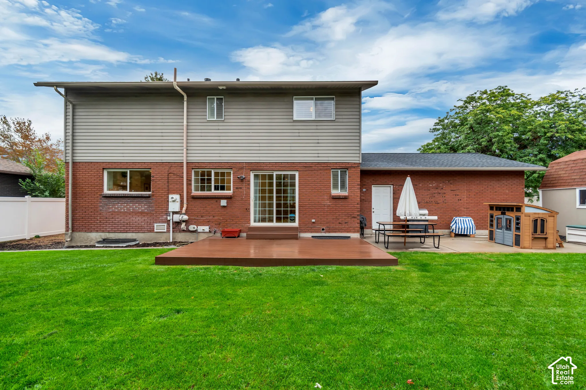 Expansive green lawn with a composite deck, brick and siding exterior, sliding glass door, and a white picket fence
