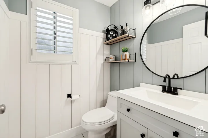 White board and batten wainscoting, white window shutters, white vanity with black hardware, black-framed round mirror, and black wall-mounted faucet