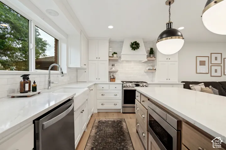 White cabinetry, stainless steel appliances, light wood-finish flooring, white subway tile backsplash, and a large central island