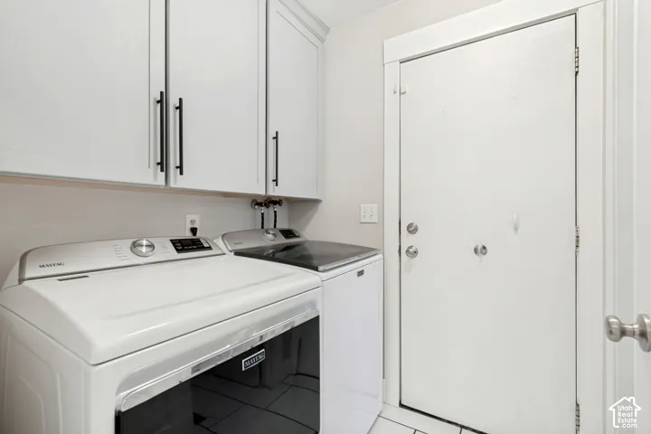 Laundry area featuring overhead cabinetry with matte black pulls, light-toned walls, and a white door with silver-toned hardware