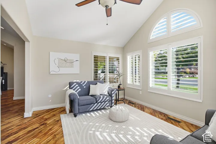 Vaulted ceiling with a ceiling fan, wood-finish flooring, plantation shutters, and a prominent arched window