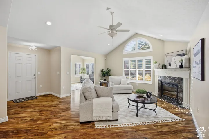 Vaulted ceiling with recessed lighting, wood-finish flooring, fireplace with stone surround, large arch window, and ceiling fan