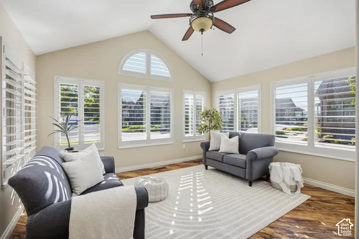 Vaulted ceiling with a ceiling fan, plantation shutters, wood-finish flooring, and multiple windows