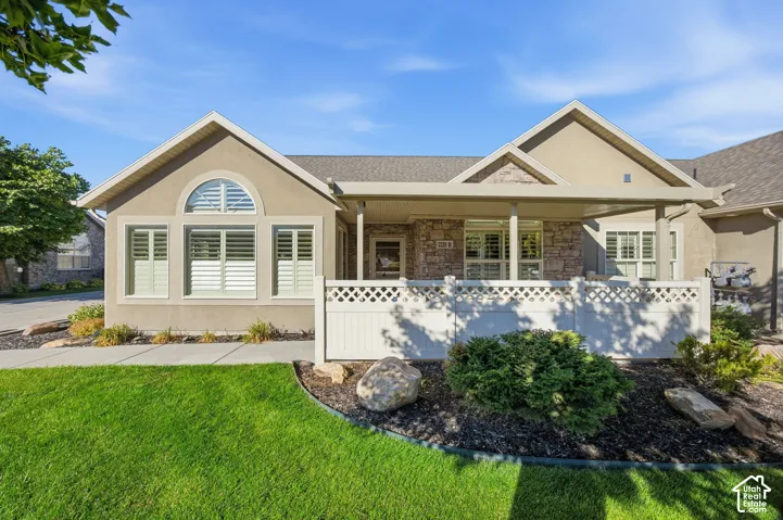 Stucco exterior with stone accents, covered front porch, arched window, and a manicured lawn with landscape rock and plantings