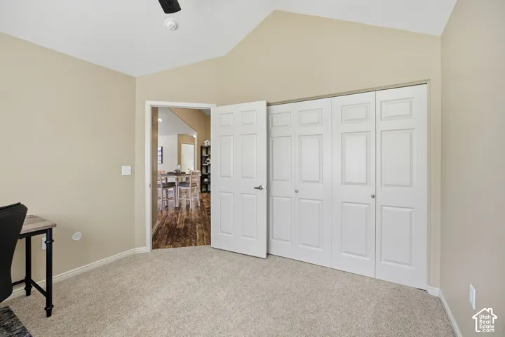 Vaulted ceiling, ceiling fan, carpeted flooring, white bi-fold closet doors, and a paneled interior door