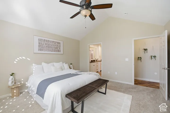 Vaulted ceiling with a ceiling fan, carpeted flooring, and a doorway revealing a bathroom with a double vanity