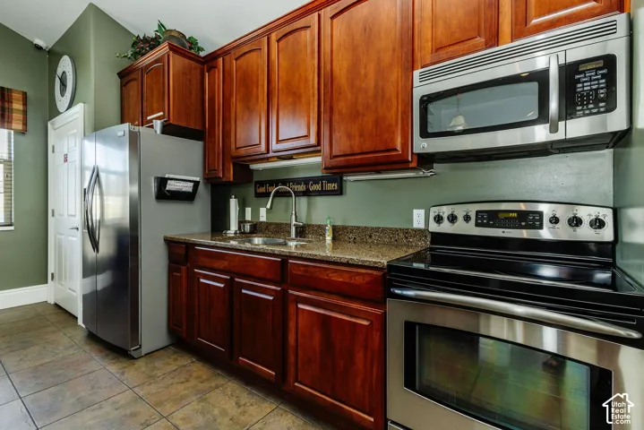 Rich wood-finish cabinetry, stainless steel appliances, speckled countertops, and durable tile flooring