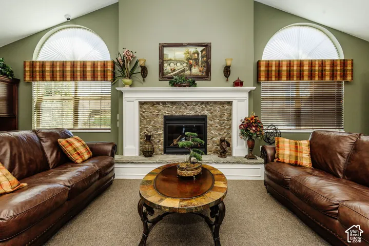 Vaulted ceiling with arched windows, central fireplace with stone tile surround, ornate white mantelpiece, and carpeted flooring