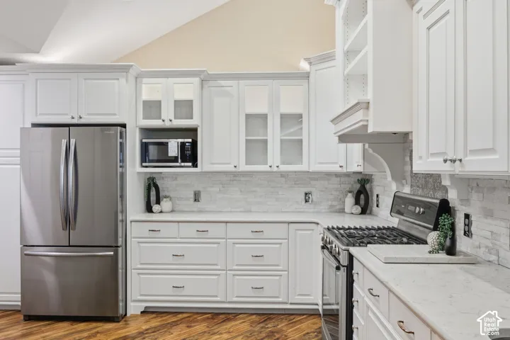White cabinetry with upper glass-front accents, stainless steel refrigerator, built-in microwave, gas range, and stone-finish countertops