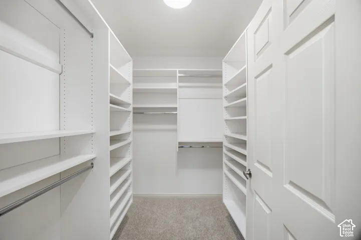 Walk-in closet featuring white built-in shelving, multiple hanging rods, recessed lighting, and carpet flooring