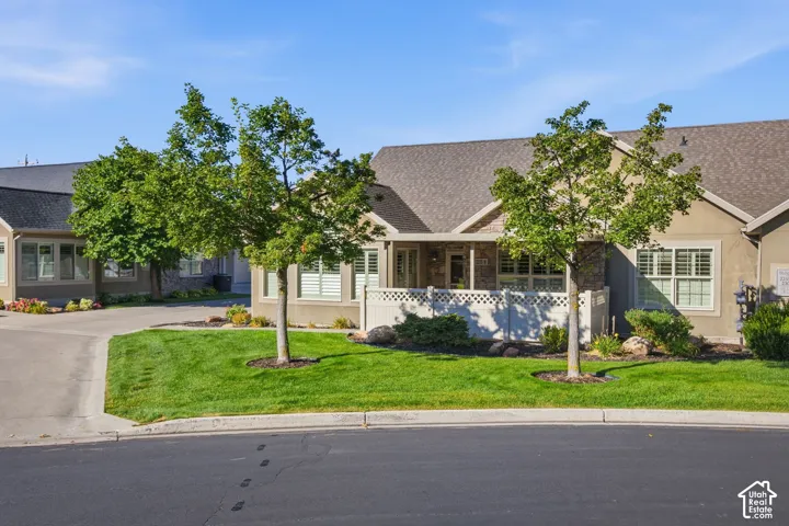 Stucco exterior with stone accents, composite shingle roof, white privacy fencing, and mature landscaping