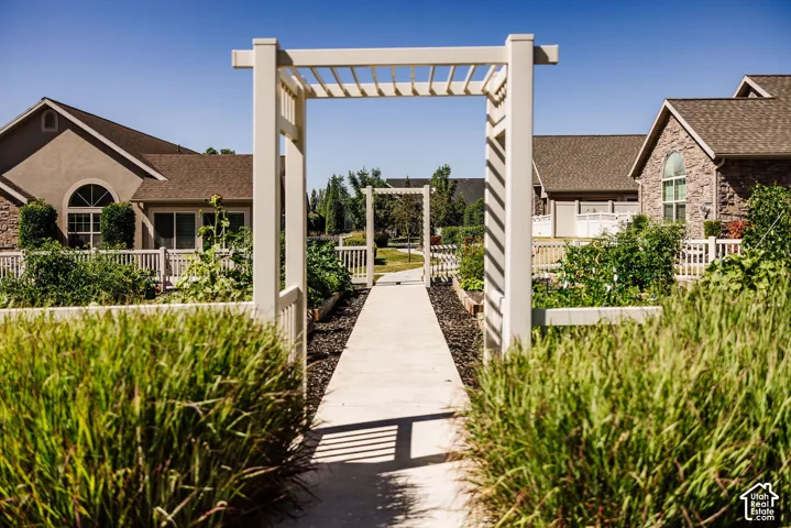 Manicured grounds featuring a paved pathway, white pergola, raised garden beds, and white picket fencing
