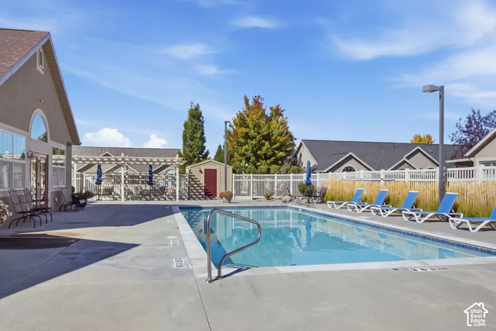 In-ground swimming pool with concrete surround, adjacent pergola, and a storage shed