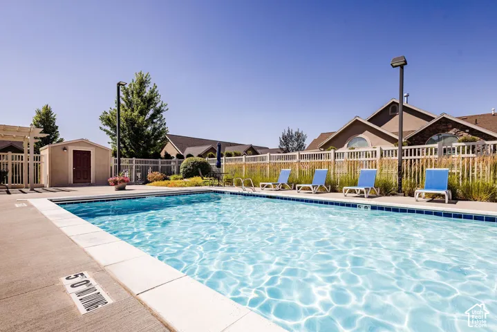 Outdoor swimming pool with a concrete surround, white fencing, and a nearby storage shed
