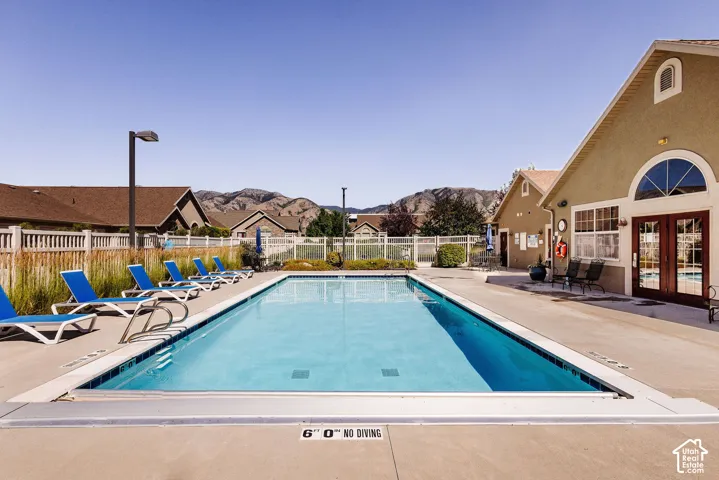Rectangular swimming pool with a concrete deck, surrounded by a light-colored building with an arched window, and distant mountains
