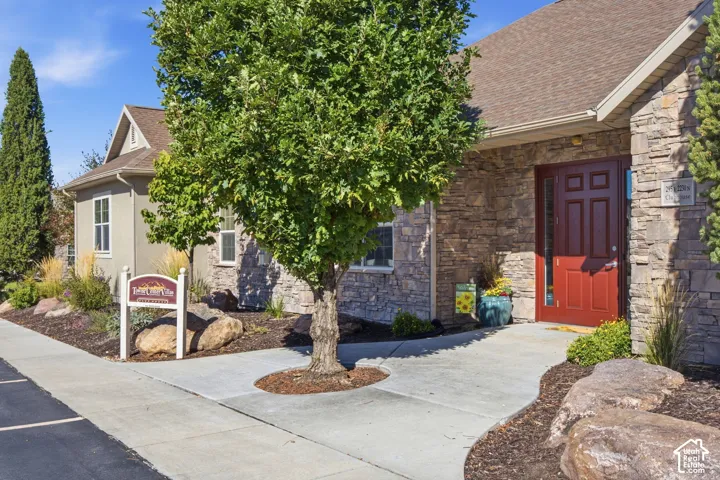 Stone facade with a red panel door, shingle roof, and concrete pathway