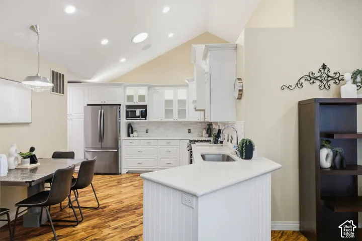 Vaulted ceiling, recessed lighting, white cabinetry, stainless steel appliances, and wood-finish flooring