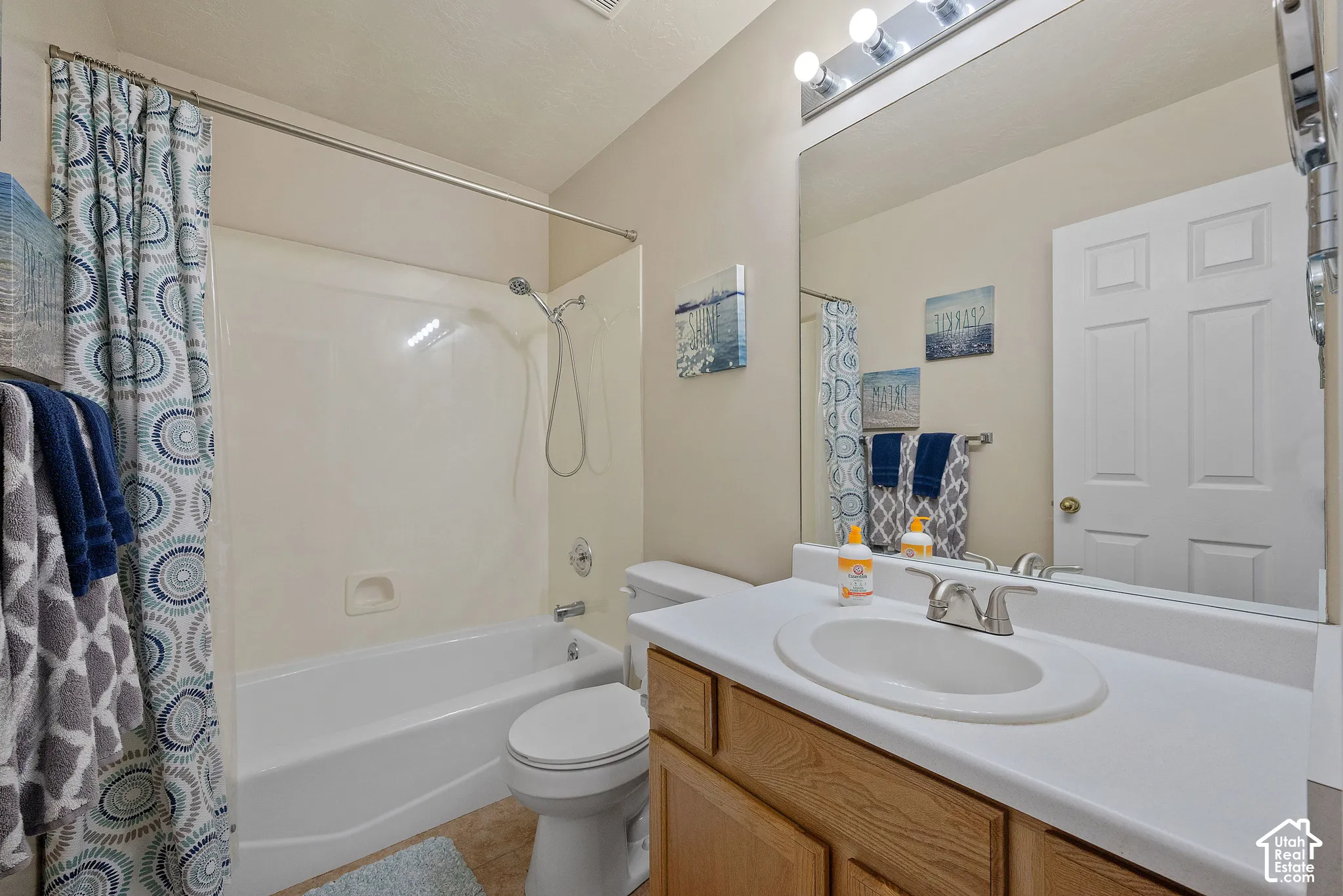 Full bathroom featuring a white tub and shower combination, a single vanity with an integrated sink, a large wall-mounted mirror, and wood-finish cabinetry