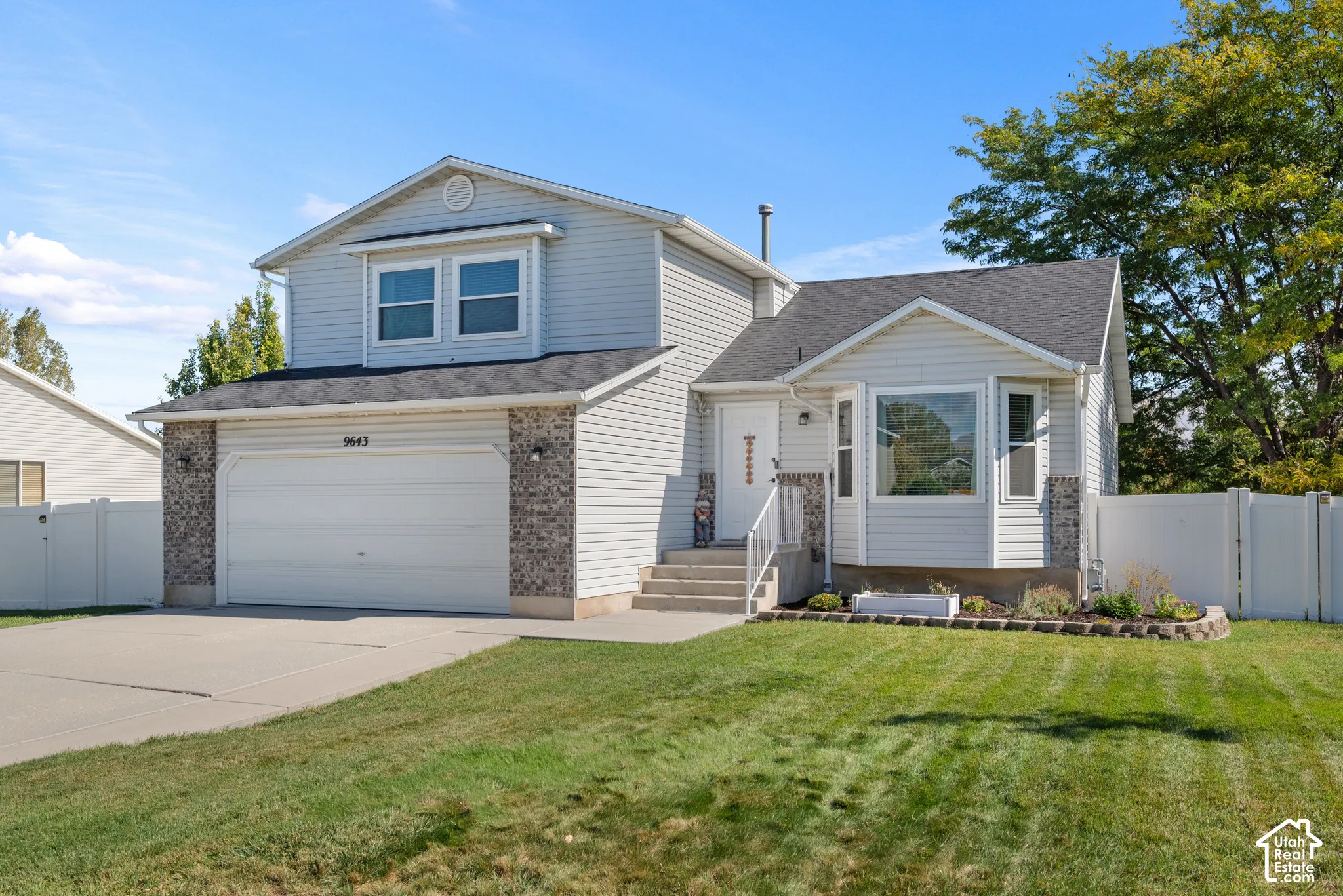 Vinyl siding exterior with stone accents, attached two-car garage, concrete driveway, and front yard landscaping