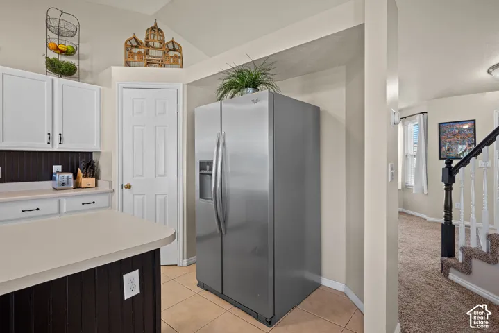 Stainless steel side-by-side refrigerator, tile flooring, white cabinetry, dark wood-paneled island base, and a white paneled door