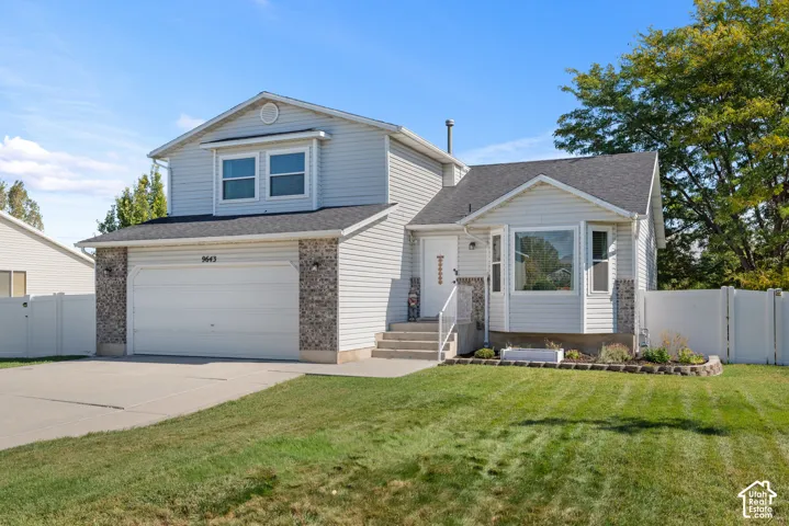 Vinyl siding exterior with stone accents, attached two-car garage, concrete driveway, and front yard landscaping