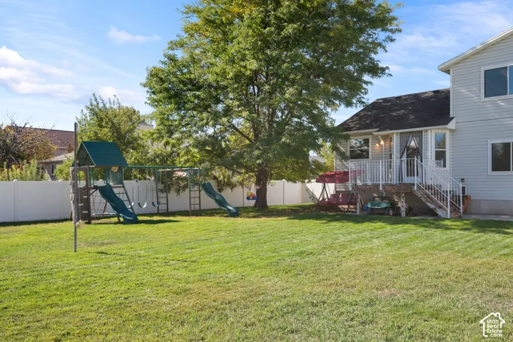 Expansive grassy yard with a white privacy fence, mature tree, and a multi-level deck with white railings