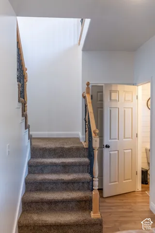 Carpeted staircase with light wood newel posts and wrought iron balusters