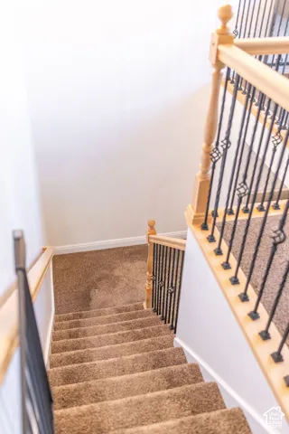 Carpeted staircase with light wood newel posts and handrails, complemented by black wrought iron balusters featuring decorative scroll accents