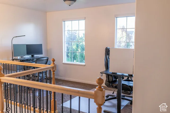 Carpeted loft area with two windows, a ceiling-mounted light fixture, and a balustrade featuring wood handrails and wrought iron spindles