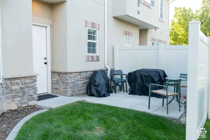 Stone veneer facade accents, private patio with concrete pavers, white privacy fencing, and a manicured lawn area