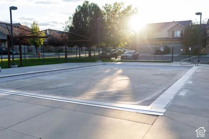 Covered swimming pool with surrounding concrete decking, metal perimeter fencing, and mature trees