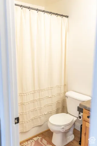 Bathroom featuring a white toilet, wood-finish flooring, and a shower area with a curtain rod