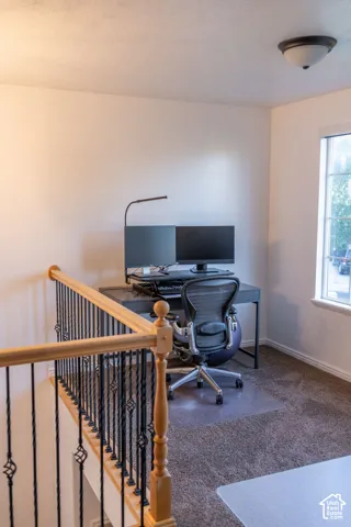 Carpeted open area with a white window frame, contemporary ceiling light fixture, and a light wood and wrought iron staircase railing