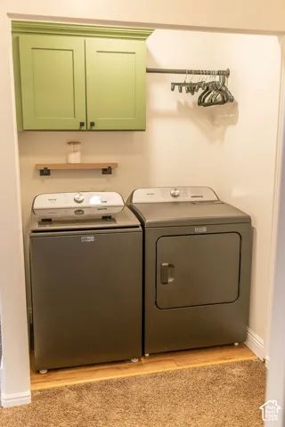 Built-in green cabinetry, wood-finish flooring, floating wood shelf, and wall-mounted hanging rod