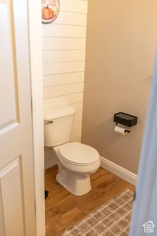 White toilet with wood-finish flooring and shiplap accent wall