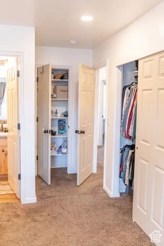 Recessed lighting illuminating a hallway with carpet flooring and multiple storage closets