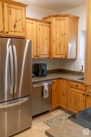 Wood-finish cabinetry with crown molding, stainless steel refrigerator, stainless steel dishwasher, and stone-finish countertops